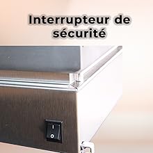 Le texte indique « Interrupteur de sécurité ». Interrupteur à bascule électrique noir monté sur un mur beige, photographié de près.