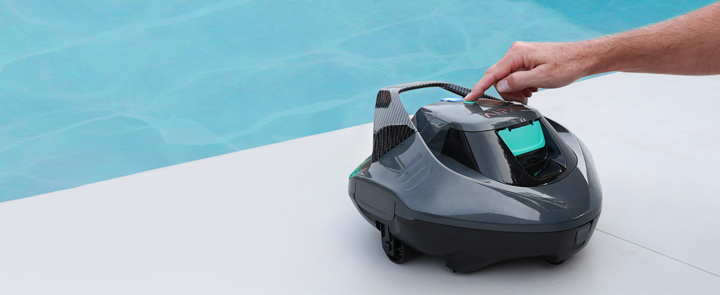La main tient un appareil compact arrondi noir avec un bouton décoratif vert sarcelle près du bord de la piscine avec de l'eau bleue visible en arrière-plan.